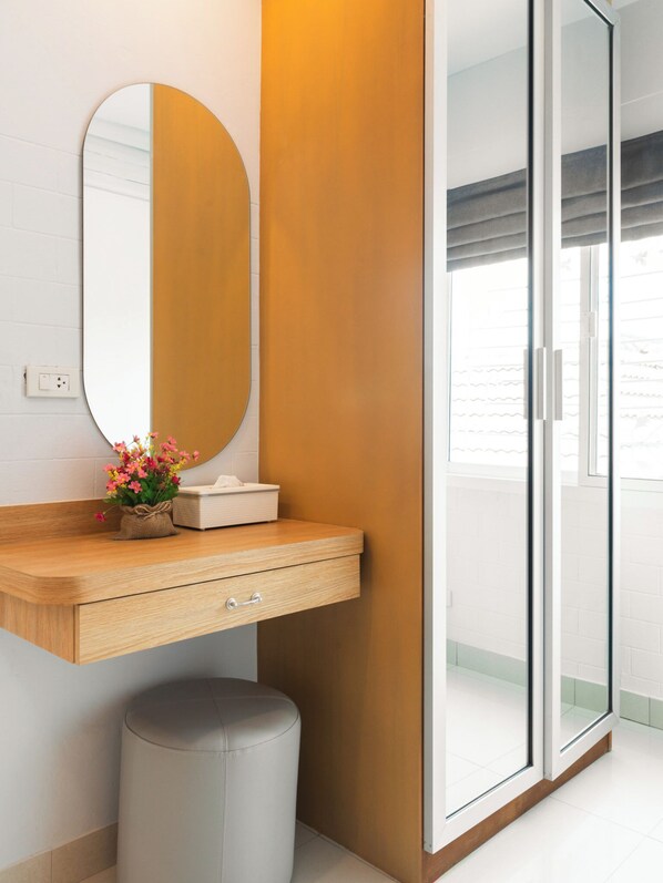 A modern bathroom with a wooden vanity, a round mirror, a small stool, and a glass shower enclosure.