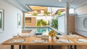 A dining area with a view of a swimming pool and a balcony.