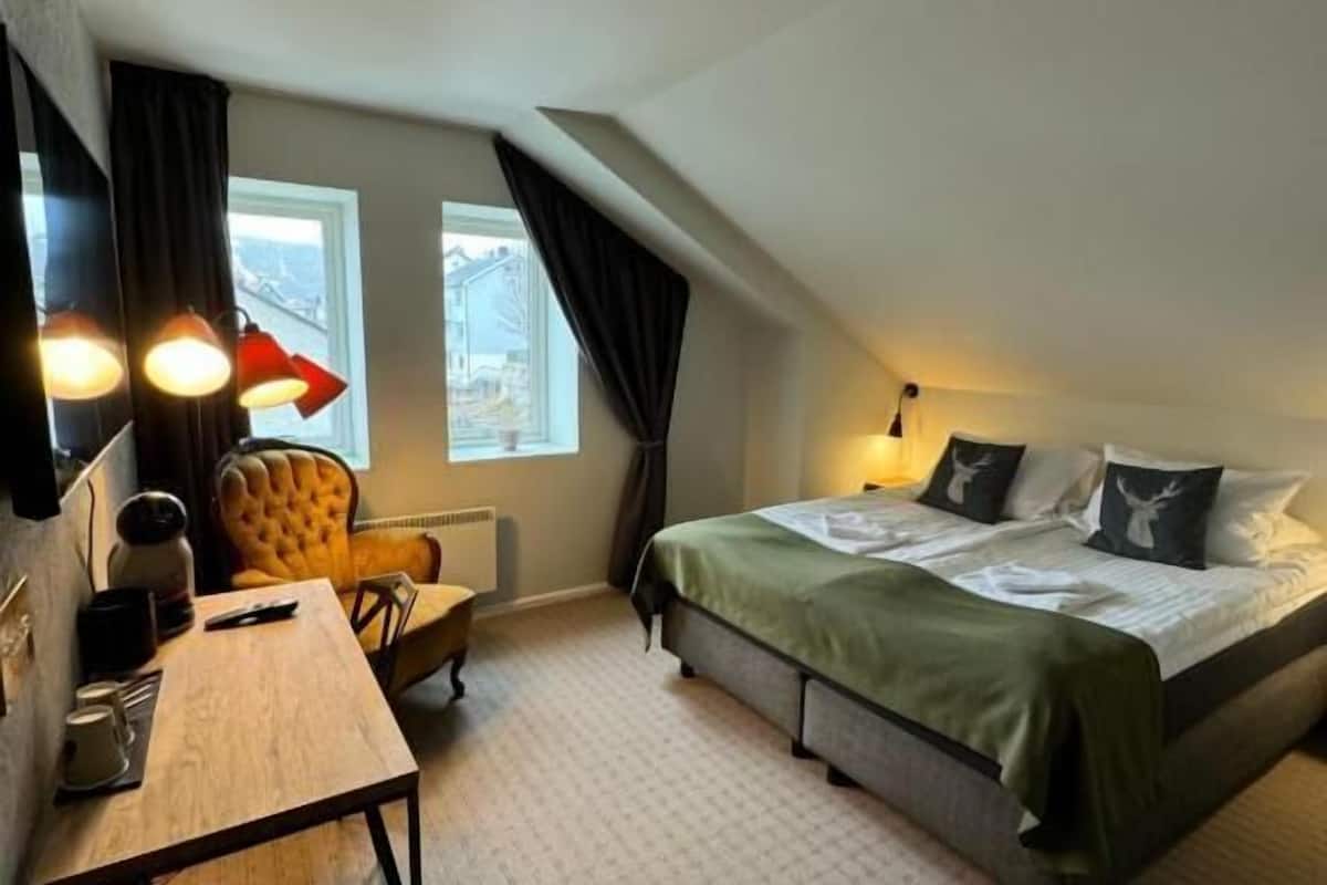 Une chambre d’hôtel avec un lit, un bureau, une chaise et une fenêtre.