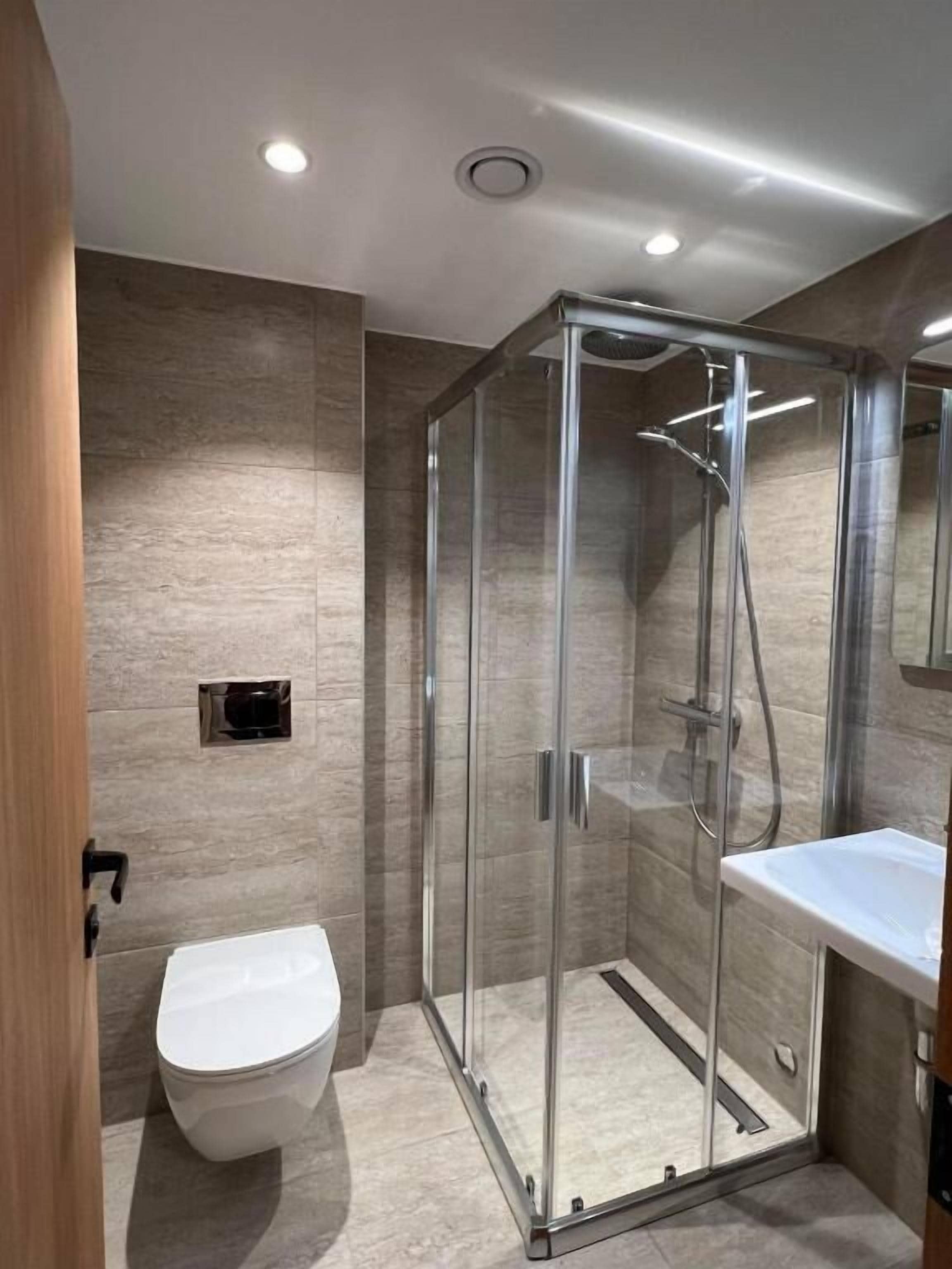Un baño moderno con ducha de vidrio, inodoro blanco y lavamanos.