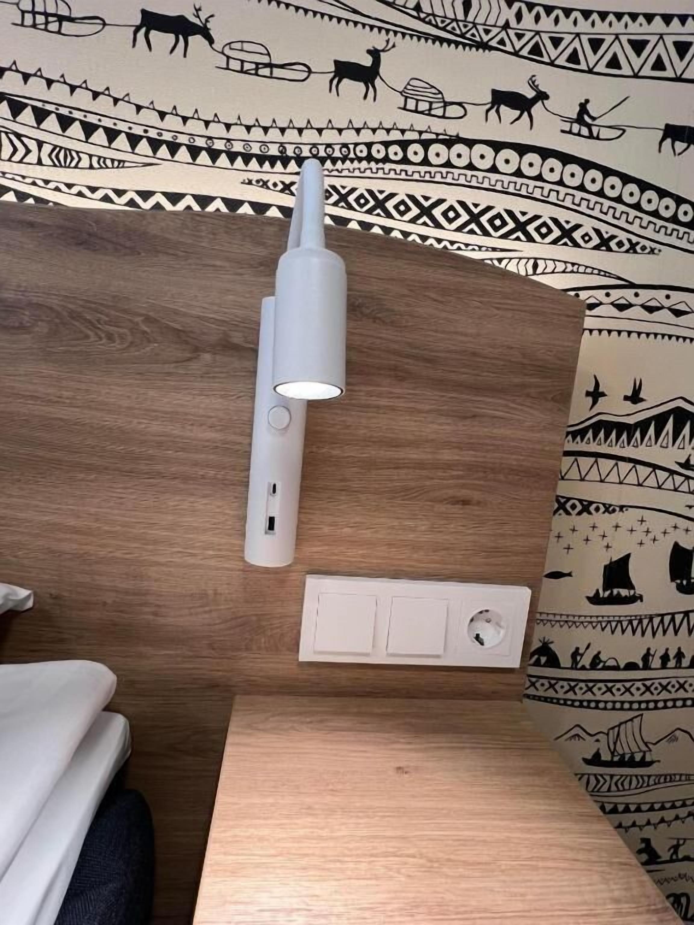 Une pièce avec un plafond en bois, un mur blanc orné de motifs tribaux, une table blanche et une lampe blanche.