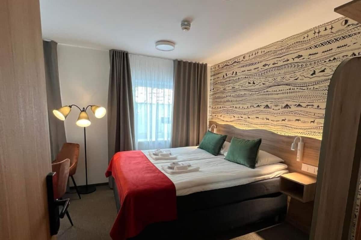 Une chambre d’hôtel avec un lit, un bureau, une chaise, une lampe et une tapisserie au mur.