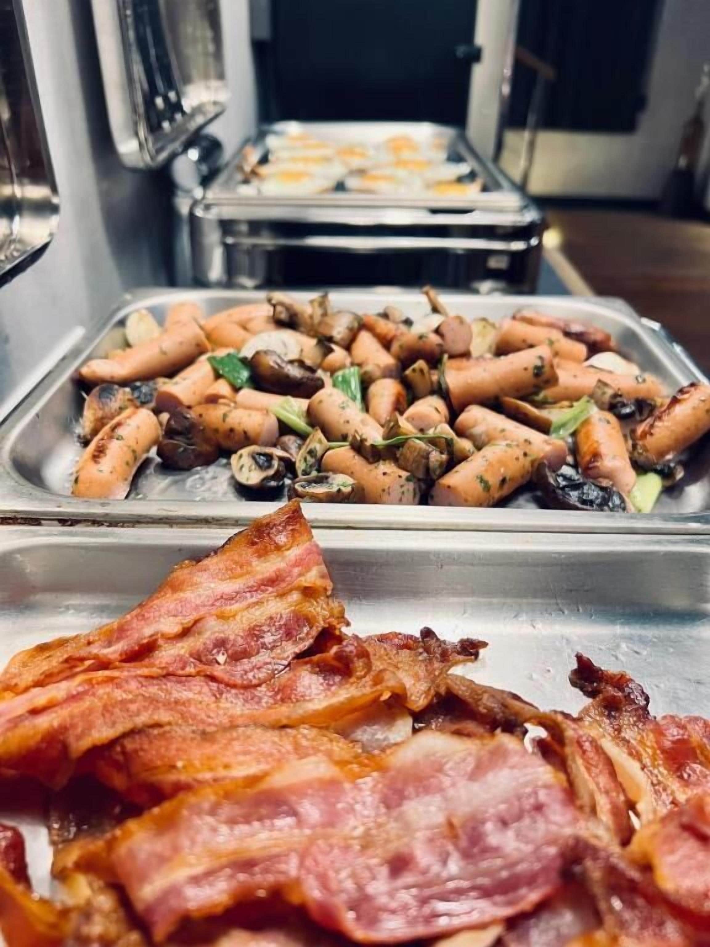A buffet with various food items including sausages, mushrooms, and bacon.