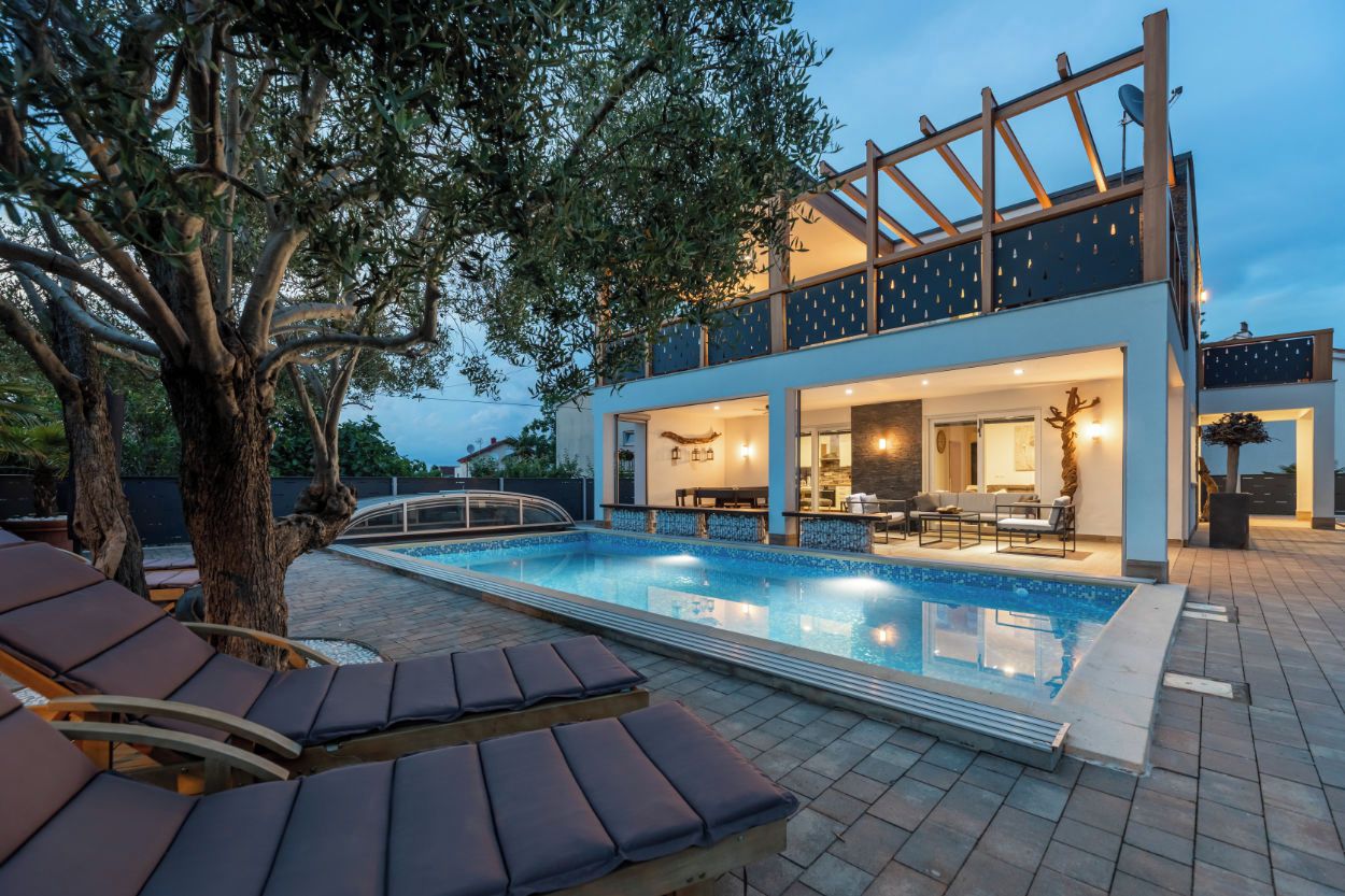 Une maison moderne à deux étages, dotée d’une piscine, d’un espace extérieur aménagé et d’un arbre.