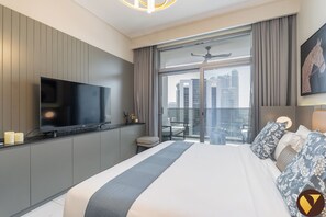 A modern hotel room with a large bed, a flat-screen TV, a balcony with a city view, and a ceiling fan.