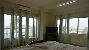 Habitación de hotel con cama, televisión y vista a un paisaje urbano a través de amplios ventanales.