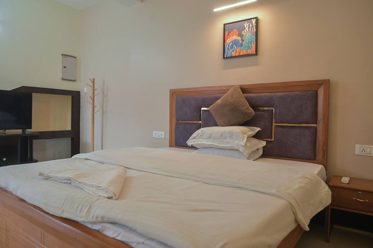 A neatly made bed with white linens, a wooden headboard, and a painting above it.