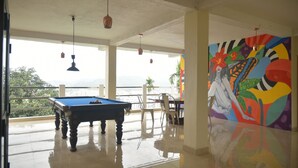 Una mesa de billar en una habitación con ventanas amplias, un mural colorido y vistas de la ciudad.