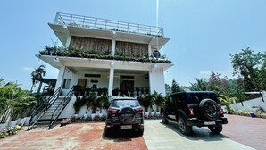 Un edificio de dos pisos con un balcón, una escalera y dos camionetas SUV estacionadas.