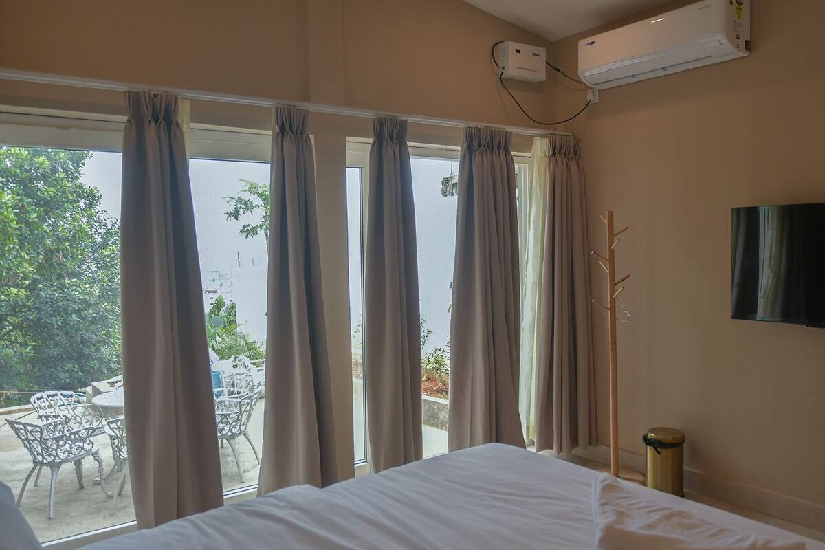 A hotel room with a bed, a TV, and a window with curtains.