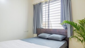 Una cama individual con cabecera de madera, ropa de cama gris y una ventana con cortinas azules.