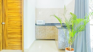 Cocina compacta con puerta de madera, microondas, encimera de mármol y una planta en maceta.