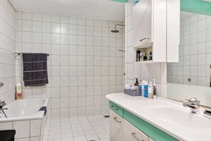 A modern bathroom with a bathtub, a sink, and a shower. There are toiletries on the sink counter. - Charming Town Apartment in Gram (Gram)