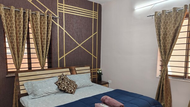 A neatly made bed with a blue quilt, a patterned pillow, and two rolled towels. - Staeg 2bhk Heart of the city (Bhopal)