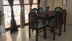 A dining area with a table and chairs, a ceiling fan, and a view of the outside through large windows with curtains. - Staeg 2bhk Heart of the city (Bhopal)