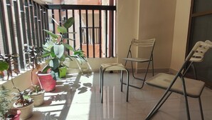 A balcony with potted plants, a chair, and a view of buildings. - Staeg 2bhk Heart of the city (Bhopal)