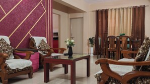 A living room with wooden furniture, a glass-top coffee table, and a decorative wall. - Staeg 2bhk Heart of the city (Bhopal)