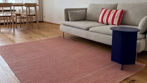 Una sala de estar con un sofá, una mesita redonda, un tapete estampado y un comedor con sillas y una mesa.