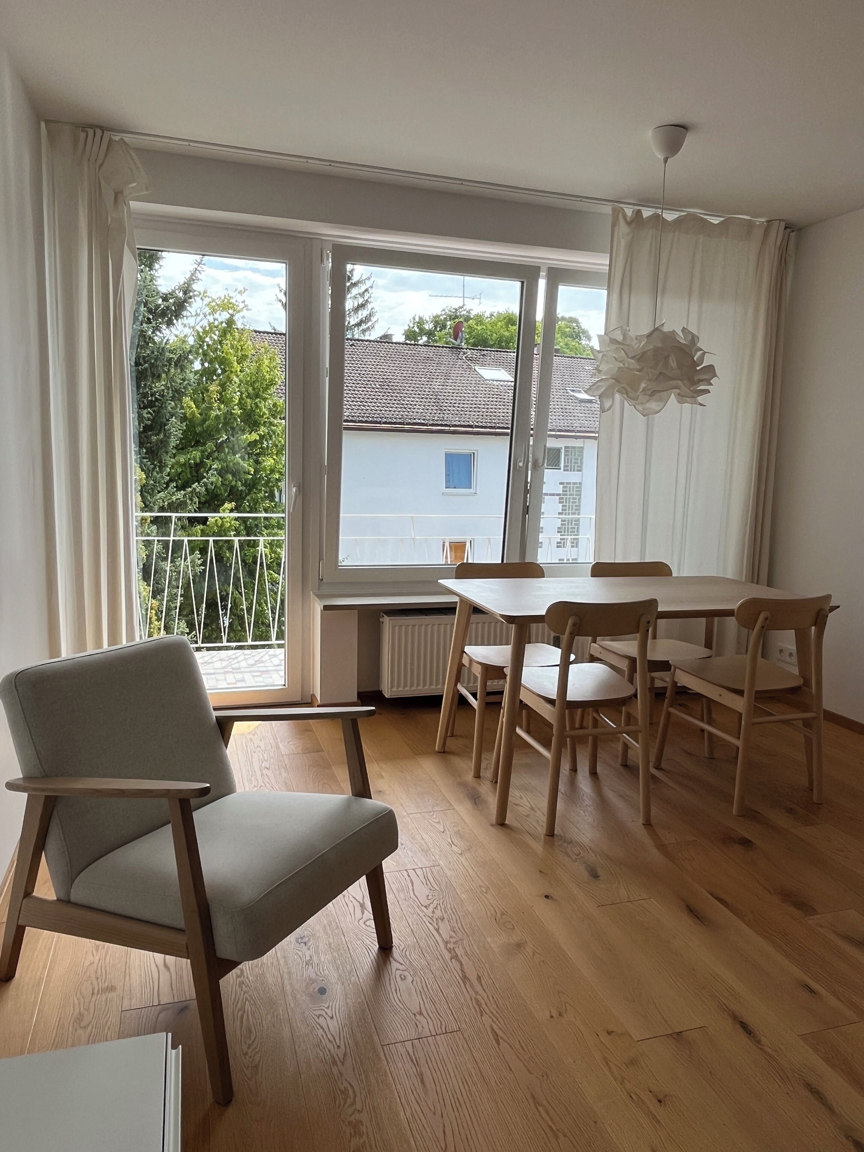 A modern living room with a dining area, large windows, and a view of the outside.