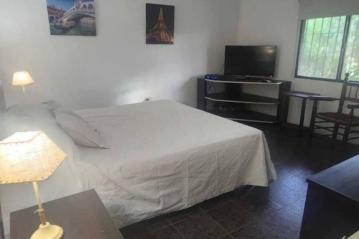 A hotel room with a bed, a TV, a desk, and a chair. There are two paintings on the wall.