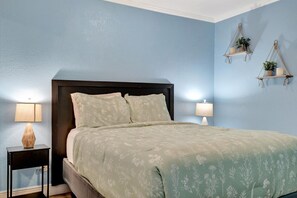 A bedroom with a bed, two bedside tables, and wall-mounted shelves with plants. - Bay View Condo w/ Heated Pool (Tampa)