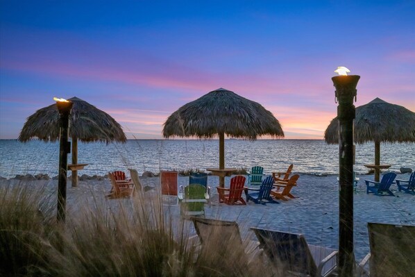 Ein Strand mit Strohdächern und bunten Adirondack-Stühlen.