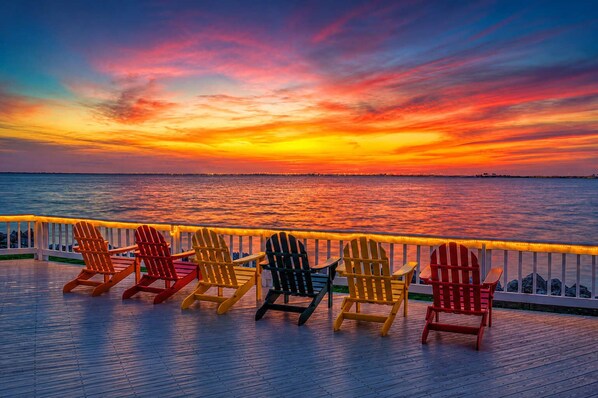 Eine Holzterrasse mit Adirondack-Stühlen, die auf den Sonnenuntergang über dem Wasser ausgerichtet ist.