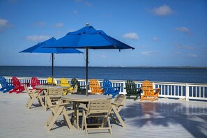 Eine Terrasse mit Sitzgelegenheiten im Freien, darunter Tische und Stühle, und zwei blaue Sonnenschirme.