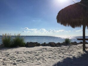 Uma praia com guarda-sol de palha, areal arenoso e mar calmo sob um céu claro.