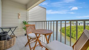 A balcony with a wooden table and chairs, a small potted plant, and a wicker basket with yoga mats. - LA Kids Suite | Waterfront w/ Heated Pool Access (Tampa)