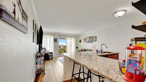 A modern kitchen with a granite countertop, a red beverage dispenser, and a dining area with a sofa and a table. - LA Kids Suite | Waterfront w/ Heated Pool Access (Tampa)