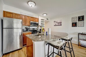 A modern kitchen with wooden cabinets, stainless steel appliances, a granite countertop, and a bar stool area.