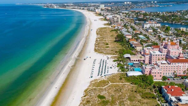 An aerial view of a coastal city with a long sandy beach, a marina, and a mix of residential and commercial buildings.