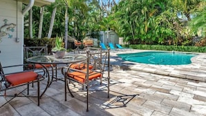 A pool area with a glass table and chairs, surrounded by palm trees and a brick patio.