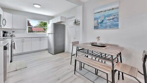 Una cocina moderna con armarios blancos, un refrigerador de acero inoxidable y una zona de comedor con una mesa y un banco de madera.