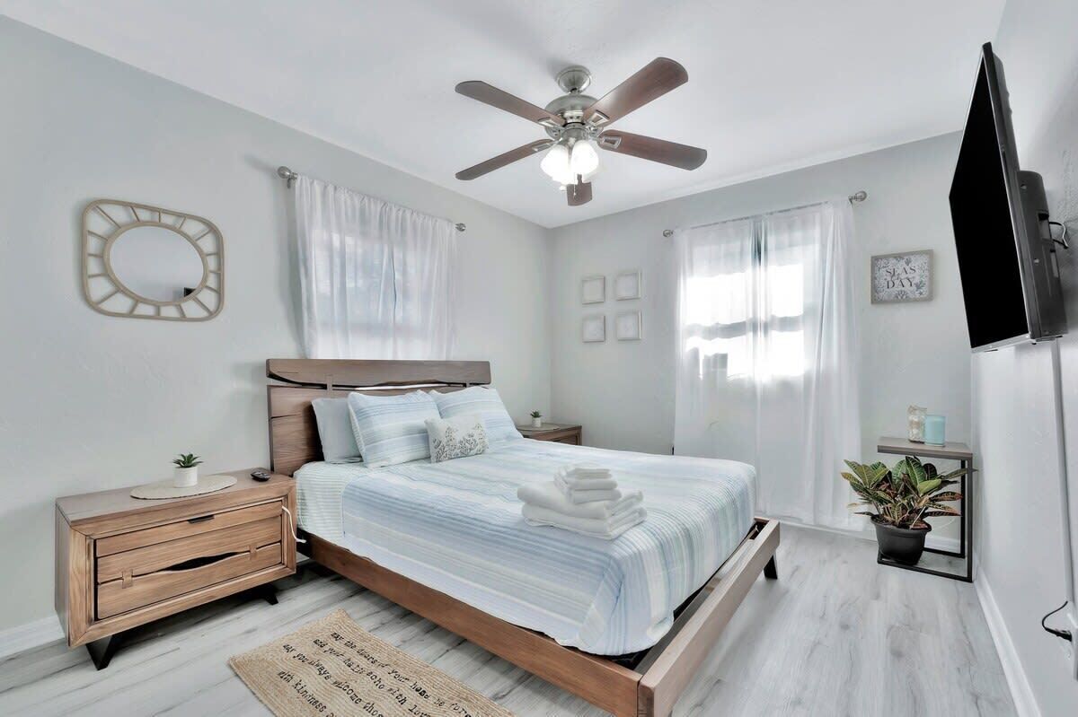 A bedroom with a bed, nightstands, a ceiling fan, a TV, and a potted plant.