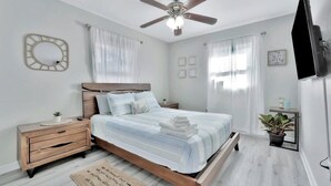 Un dormitorio con cama, mesitas de noche, ventilador de techo, televisión y una planta en maceta.