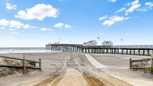Een strand met een houten pier die naar een gebouw leidt, met een bord waarop 'OCFC' staat.