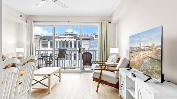 Een moderne woonkamer met balkon, witte meubels en een grote televisie waarop een strandscène te zien is.