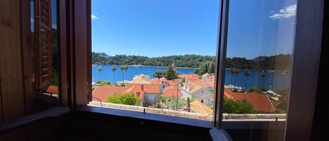 A room with a large window overlooking a coastal town with red-roofed buildings and a clear blue sky.