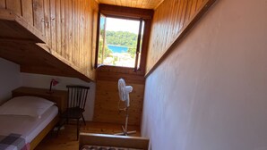 Una pequeña habitación de cabaña de madera con una cama individual, una silla y un ventilador.