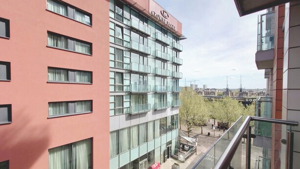 Un edificio a più piani con un cartello ben visibile 'Crowne Plaza', ampie finestre e una zona esterna con posti a sedere.