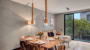 Un espace de repas moderne avec une table en bois dressée pour quatre personnes, un canapé et une grande fenêtre donnant sur un paysage verdoyant.