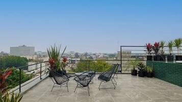 Une terrasse sur le toit avec trois chaises, des plantes en pot et une vue sur la ville.