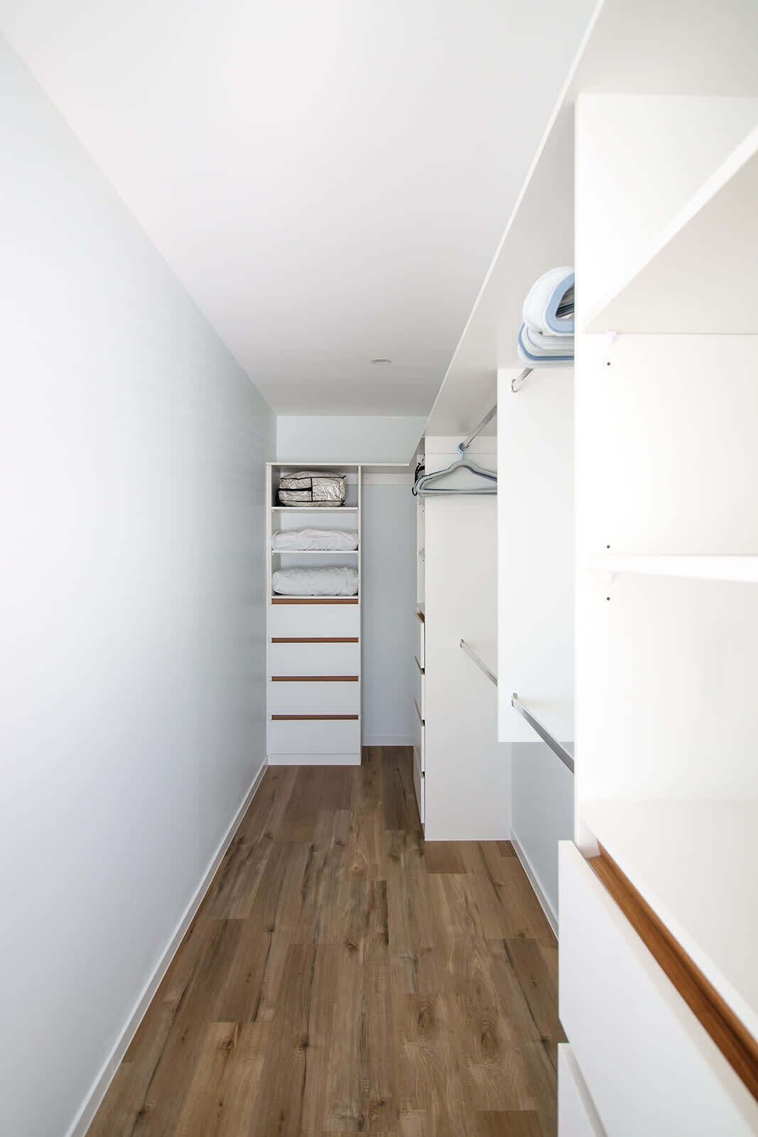 A narrow hallway with wooden flooring, white walls, and a closet with hanging space and shelves.