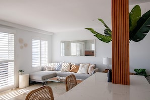 Un salon moderne avec un canapé, une table basse et une table à manger. Un grand miroir est accroché au mur et une plante est placée dans un coin.