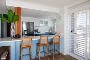 Une cuisine moderne avec un îlot central, des tabourets de bar, une grande plante et une vue par la fenêtre.