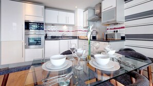 Una cocina moderna con armarios blancos, electrodomésticos de acero inoxidable y una mesa de vidrio con capacidad para seis comensales.