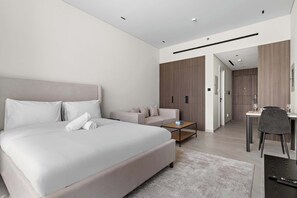 A modern hotel room with a large bed, a sofa, a desk, and a chair.