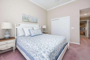 Une chambre à coucher comprenant un lit, deux tables de chevet, une commode, une porte et un couloir menant à une autre pièce.